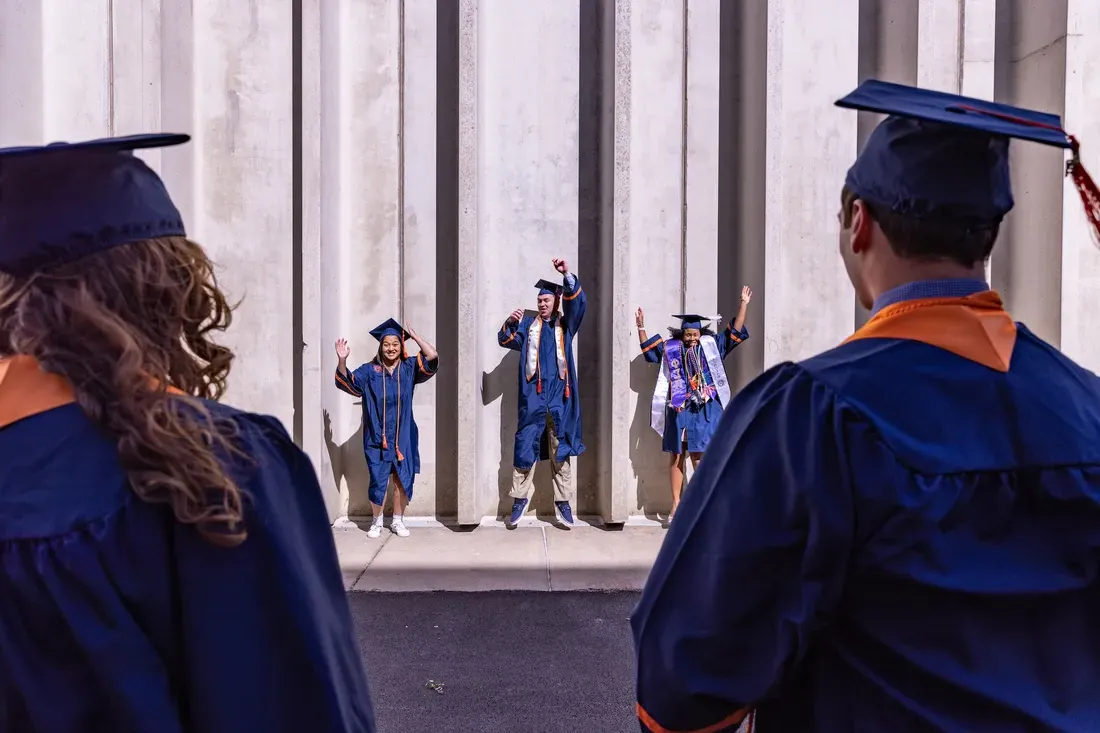 Students jump outside the Dome in their graduation caps and gowns.